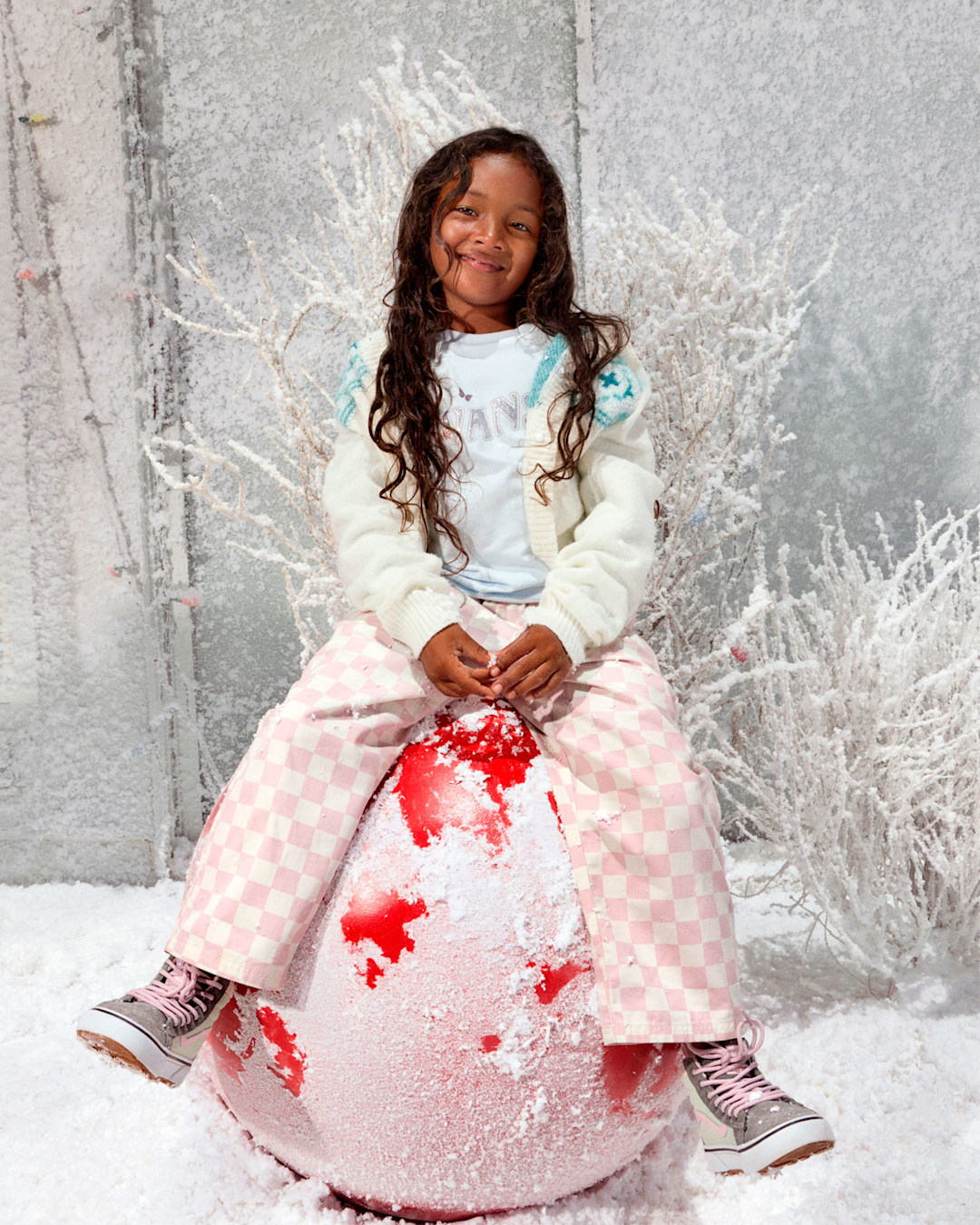 Kids' holiday apparel featuring pink checkerboard pants, a graphic T-shirt, and Vans sneakers in a winter-inspired setting with the text "Gifts for Kids."
