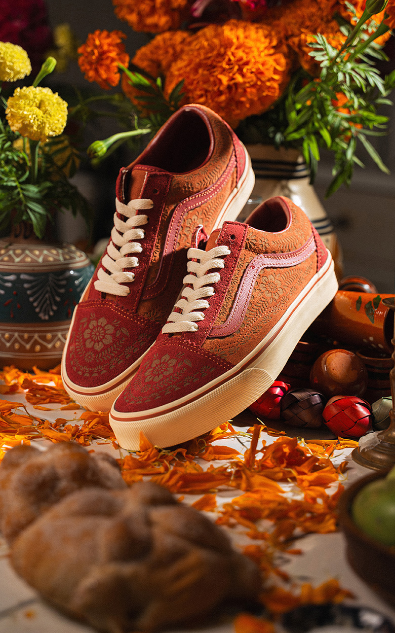 A pair of orange lace flower-patterned shoes from the Vans and Mauro Garfias collection lie on a table of marigold petals and candles.