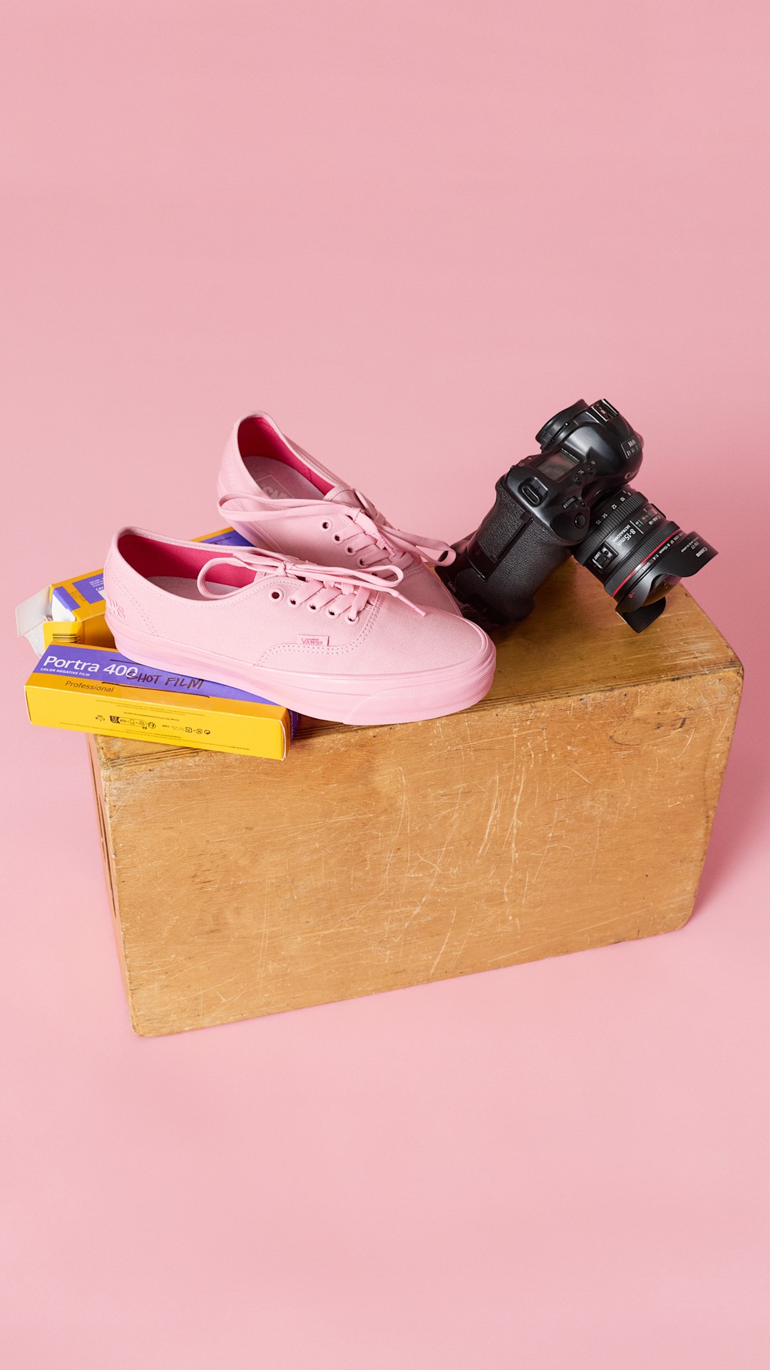 Light pink Vans Authentic shoes are displayed on a wooden box beside a professional camera and boxes of Kodak Portra 400 film. The scene is set against a soft pink background and highlights the Atiba collection's connection to photography and skate culture.