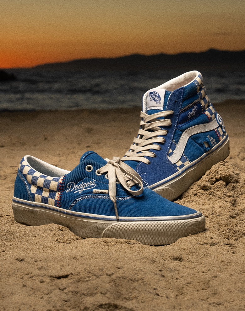 An Authentic and Sk8-Hi lie in the sand on a beach from the Vans, MLB, and Los Angeles Dodgers collection.