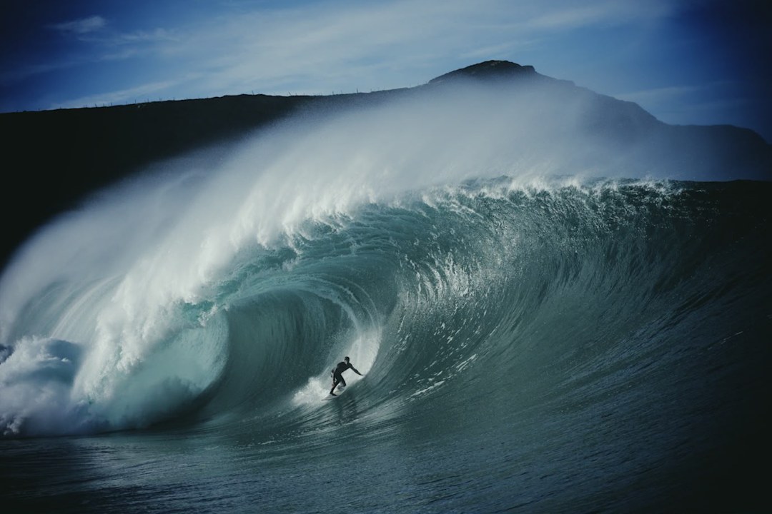 Tom Lowe riding inside the barrel of a huge wave beneath a dark headland