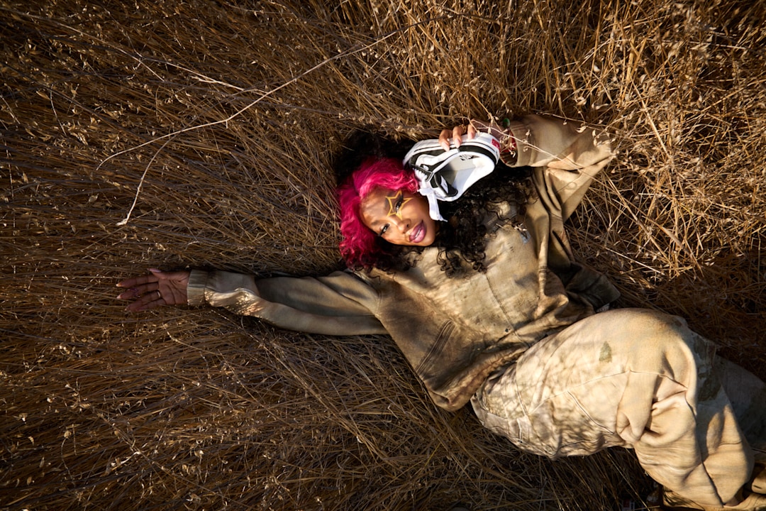 SZA laying down in a field wearing Vansza Workwear Trompe L'Oeil Fleece Set with a Vansza Knu Skool Mule in hand.