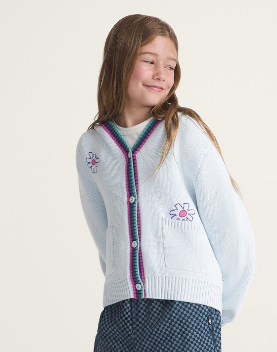 A young girl wearing a white cardigan with stitched florals in a photo studio.