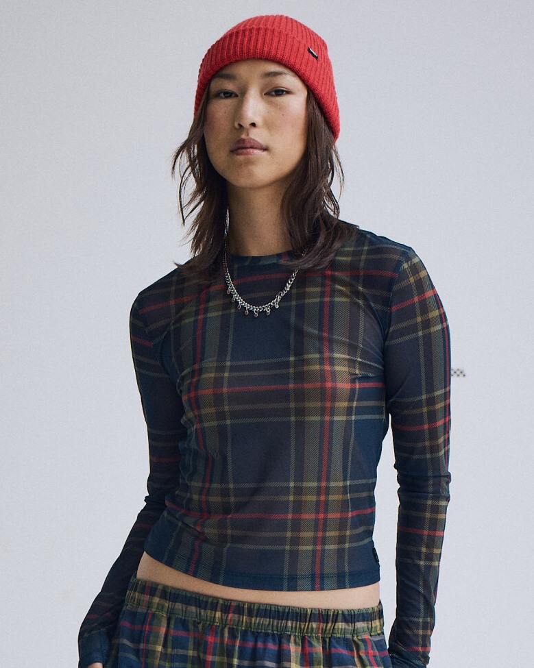 Person wearing a red, green, and navy plaid sheer long sleeve against a light gray background. The image includes the text 'Plaid.'"