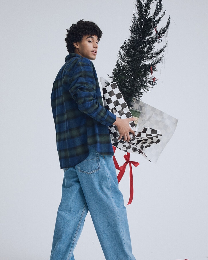 Person wearing a red and black flannel shirt with wrapped holiday gifts overhead.