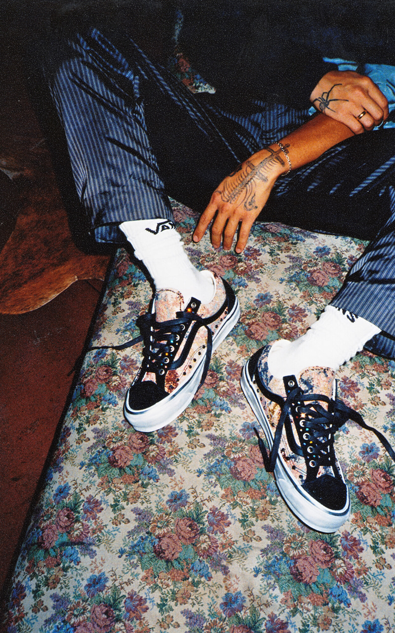 Close-up on a young man wearing Premium Old Skool 36 with florals and rivets and white Vans crew socks on a floral rug.
