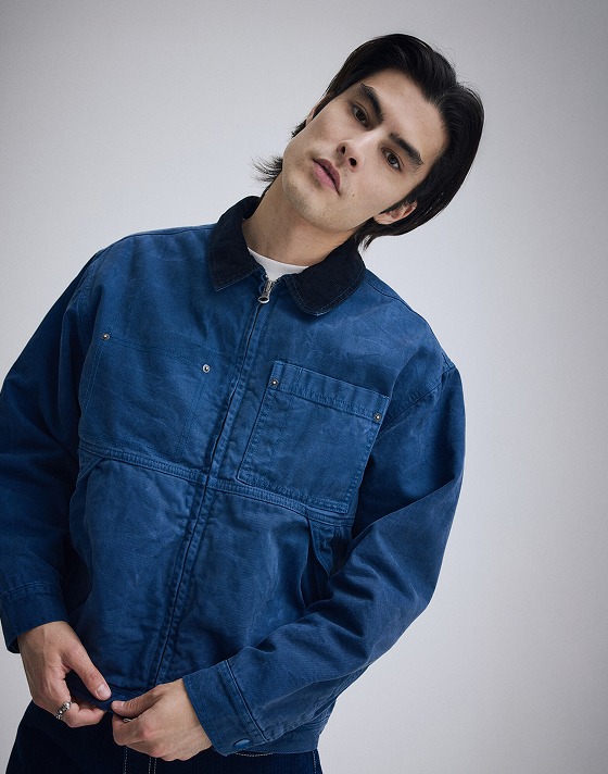 A young man wearing a blue Nico Cropped Chore Canvas Jacket in a photo studio.