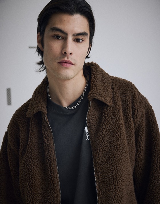 A young man wearing a brown jacket in a photo studio.