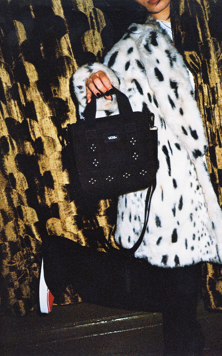 Close-up on a young woman holding a black Studded Lil Pergs Tote Bag against a gold velvet curtain.