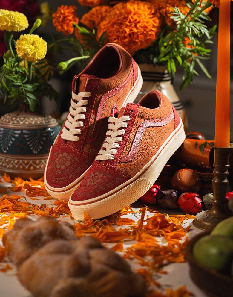 A pair of orange lace flower-patterned shoes from the Vans and Mauro Garfias collection lie on a table of marigold petals and candles.