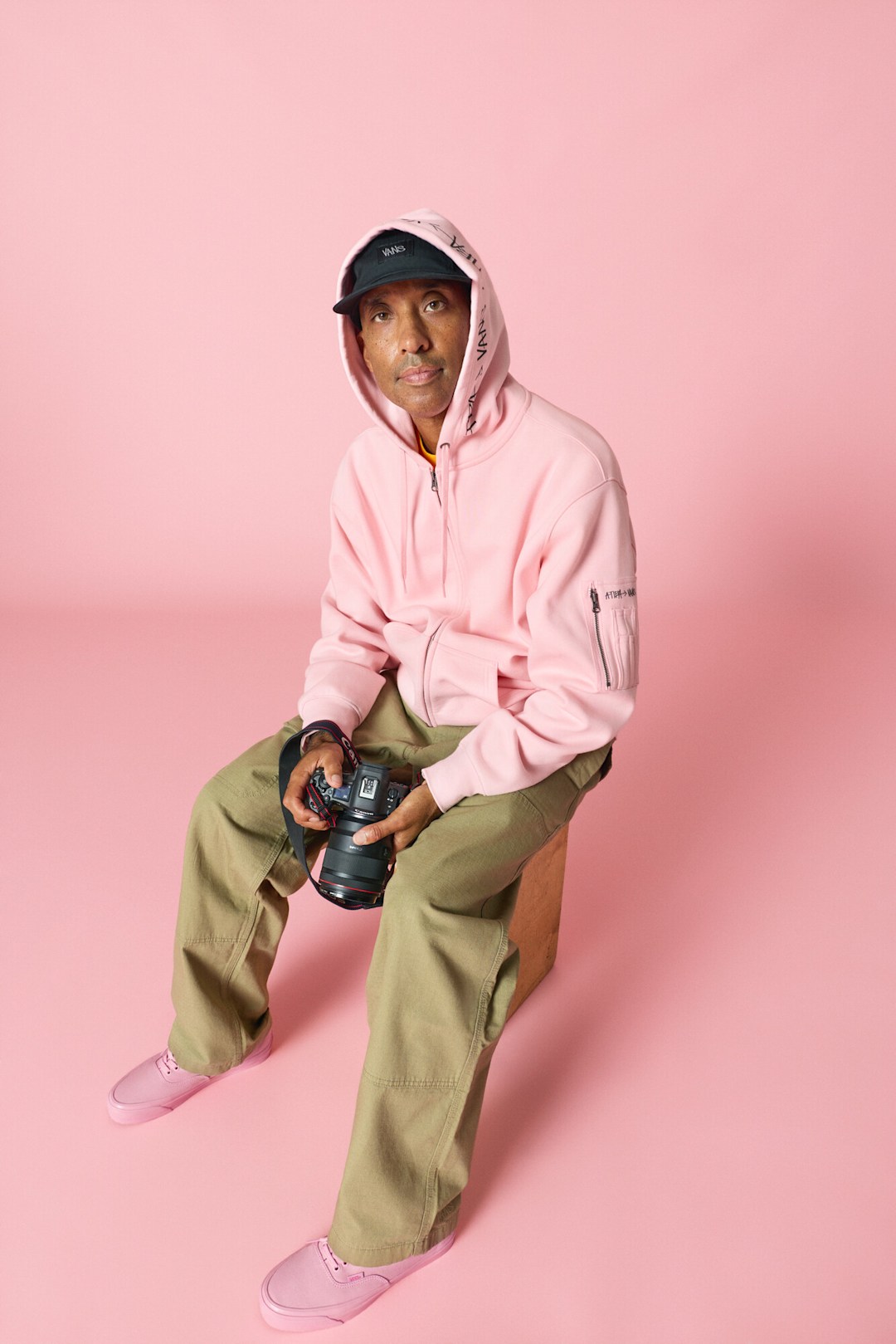 Atiba Jefferson sitting down wearing Vans x Atiba Cargo Hoodie, Premium Authentic Shoe by Atiba in pink, and Vans x Atiba Cargo Pant.