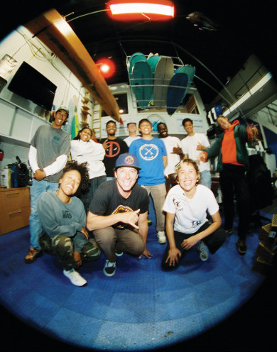 Vans athletes and professional surfers smile in a surf shop surrounded by other surfers.