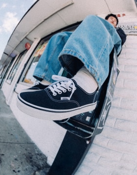 A close-up of Authentic low top shoes on a man wearing blue jeans and sitting on a public phonebooth.
