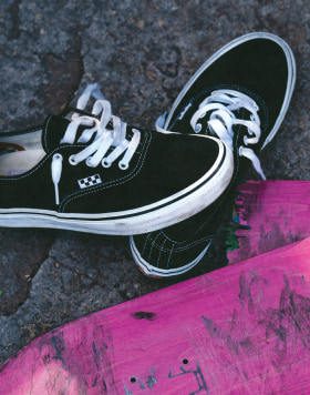 An overhead shot of two black and white Vans Skate Authentic, one on the ground untied and one on someone's foot.