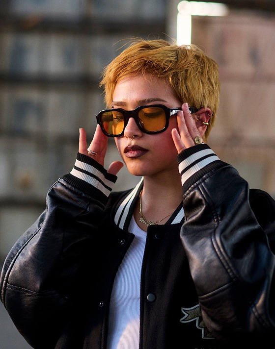 A women wearing a vans varsity black jacket and yellow frame glasses