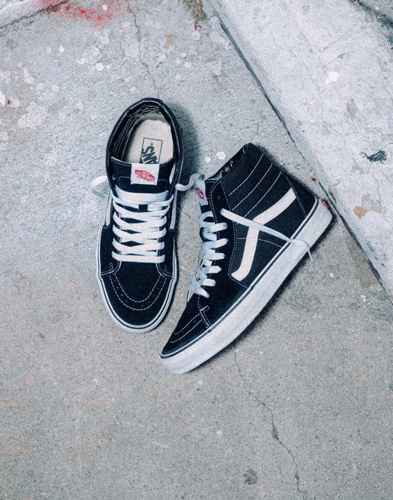 A pair of black Sk8-Hi shoes with a white SideStripe laying on the concrete.