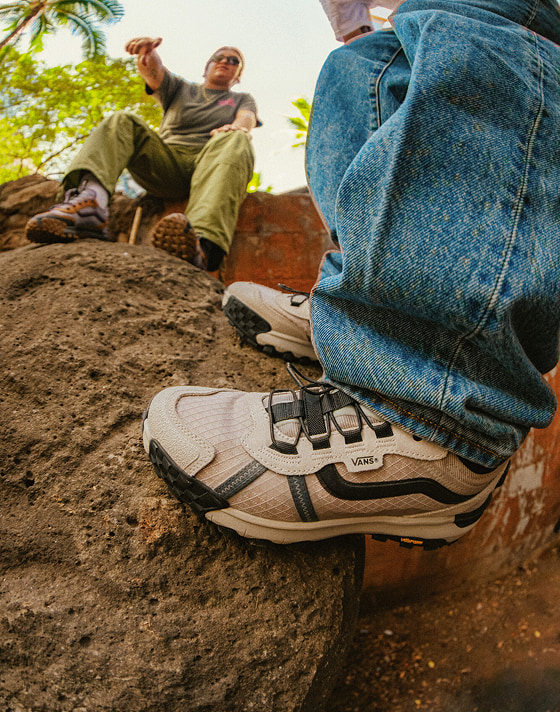 A close-up of black and white MTE Crosspath XC shoes on some rocks styled with baggy blue jeans.
