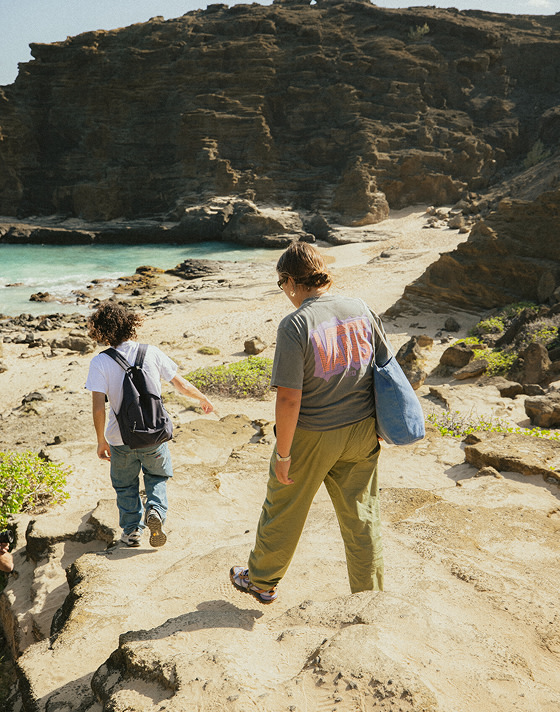 Two people walk down to a rocky beach under a cliff with backpacks and bags in MTE Crosspath XC shoes on a sunny day.
