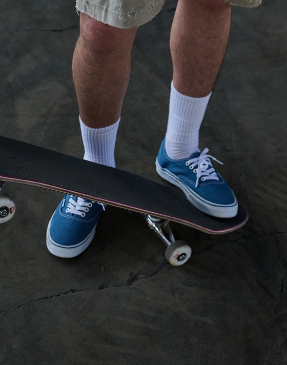 Person wearing bA person wearing blue Authentic shoes and white socks with one foot on a skateboard.lack and white checkerboard slip-ons in an urban setting.