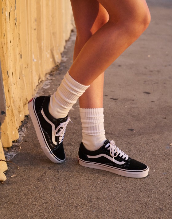 A pair of black and white Old Skool paired with white socks on a person standing on the beach.