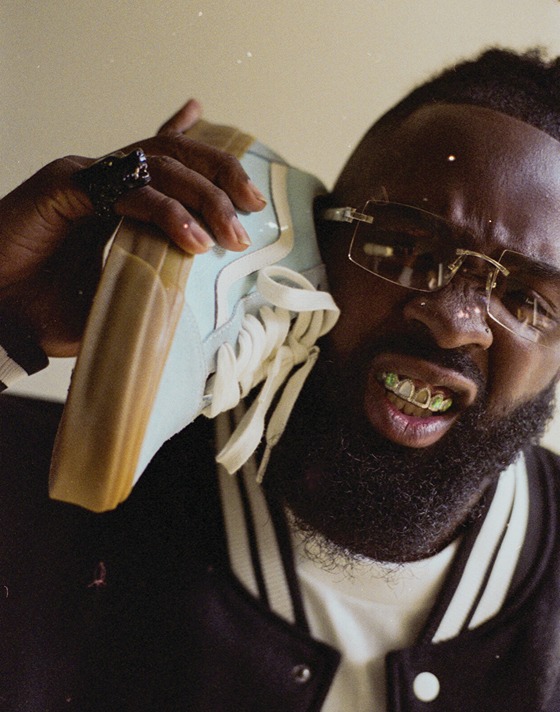 A member from the Hip-Hop/Rap band Hi-Tech holds a Crystal Blue Premium Old Skool shoe close to their face.