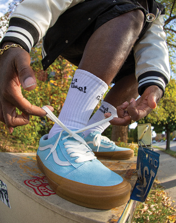 A close-up of a person lacing up Crystal Blue Premium Old Skool shoes while wearing white socks, set against an autumn backdrop.