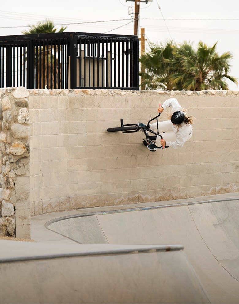 A full shot of a cyclist in protective gear performs a wall ride on a BMX bike at a skatepark.