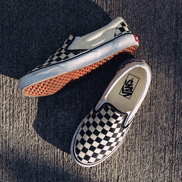 A pair of Classic Slip-On Checkerboard shoes on textured grey flooring. 