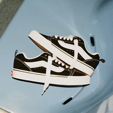A pair of Black/White Knu Skool Suede shoes placed on a light blue chair. 