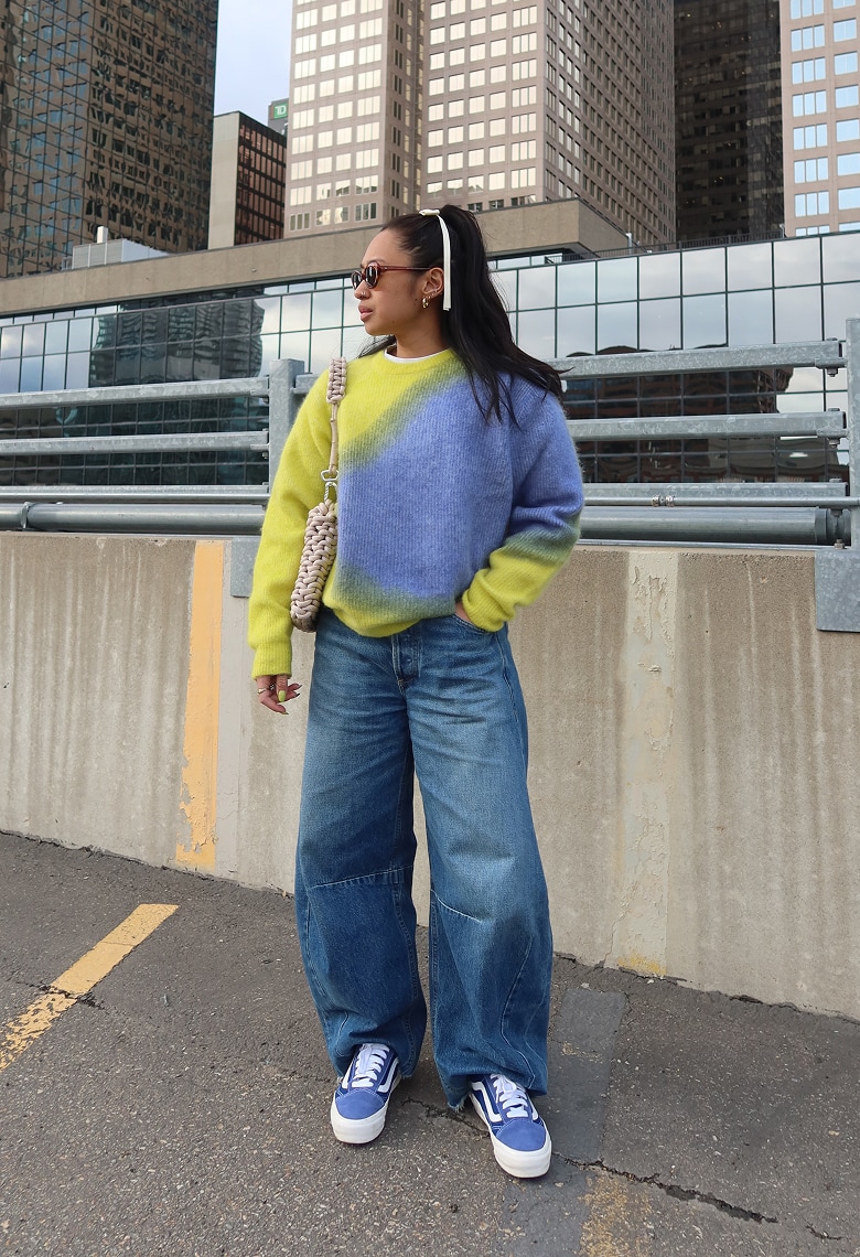 A person stands outdoors wearing oversized clothing and Old Skool shoes. 