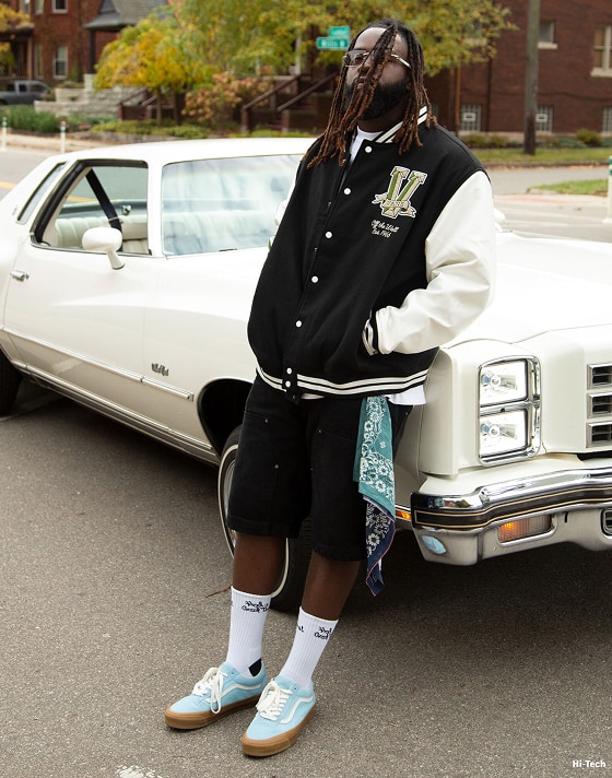 A person standing against an old car wearing blue premium old skool shoes