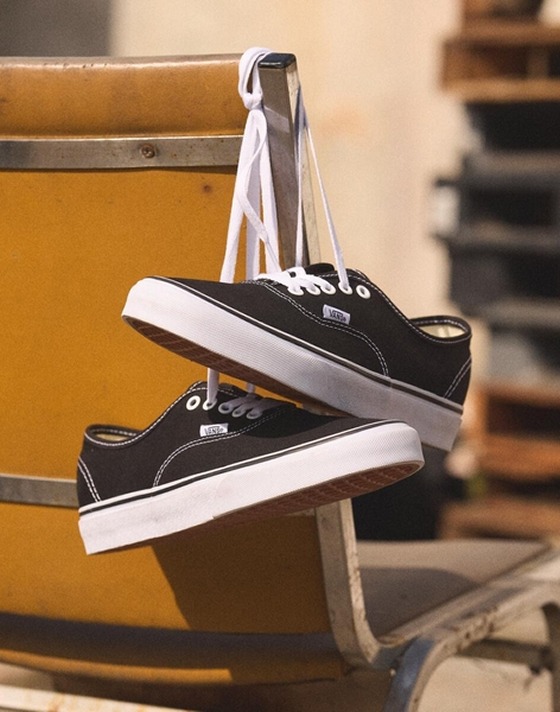 A close-up of a black pair of Authentic shoes hanging by the laces on a chair.