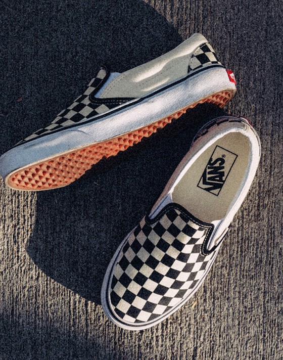 A pair black and white Checkerboard Slip-On shoes on concrete.