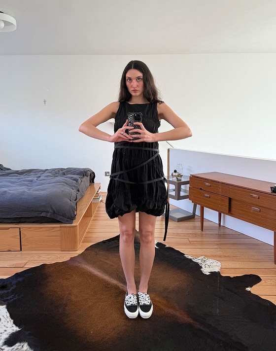 A girl taking a mirror selfie in a black dress and Premium Authentic shoes in a bedroom.