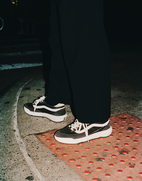 Close-up of a person wearing UltraRange 2.0 shoes at a street corner, captured at night with the shoes sharply illuminated by a camera flash.