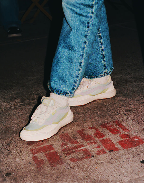 Close-up of a person wearing UltraRange 2.0 shoes at a street corner, captured at night with the shoes sharply illuminated by a camera flash.