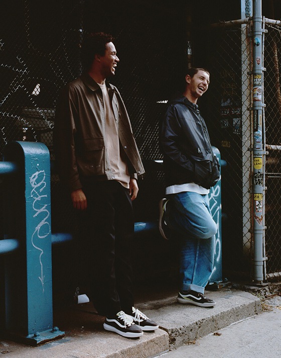 Two young men relax near an alleyway, wearing UltraRange 2.0 shoes paired with jeans and light jackets, surrounded by the casual energy of the city.