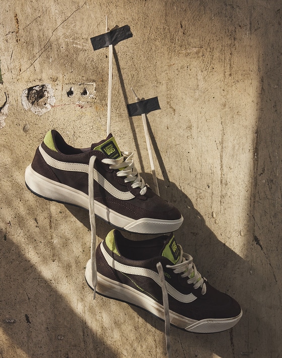 A pair of UltraRange 2.0 shoes hang by their laces, taped to a rough concrete wall, creating a bold, urban display.