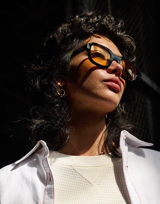 A close-up of a woman in the white Gillian Button Up Shirt and 66 Sunglasses.