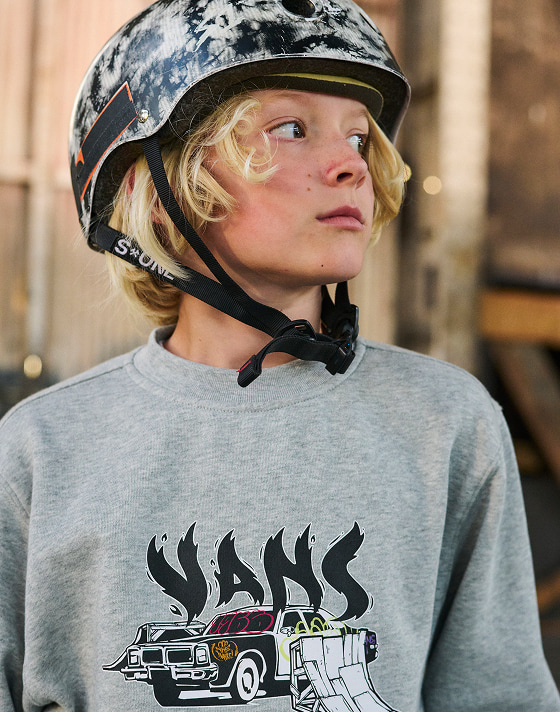 A close-up of a boy in a gray Vans pullover in a skateboarding helment.