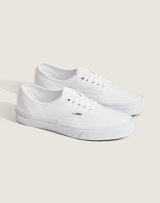 Side view of a pair of white Authentic shoes, styled against an off-white backdrop in a photography studio, showcasing their classic look in crisp detail.