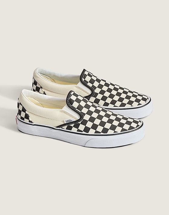 Side view of a pair of black and white checkered Classic Slip-On shoes, styled against an off-white backdrop in a photography studio, showcasing their iconic pattern in crisp detail.