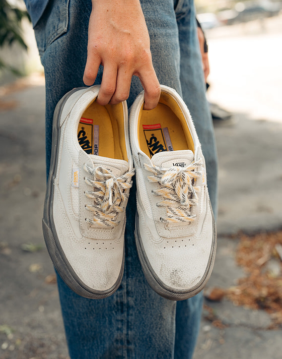 A person holding a gray pair of Curren shoes by the insides next to their leg.