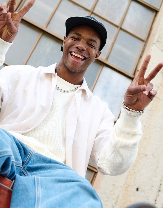 A man smiles and puts up peace signs wearing Vans Clothes.