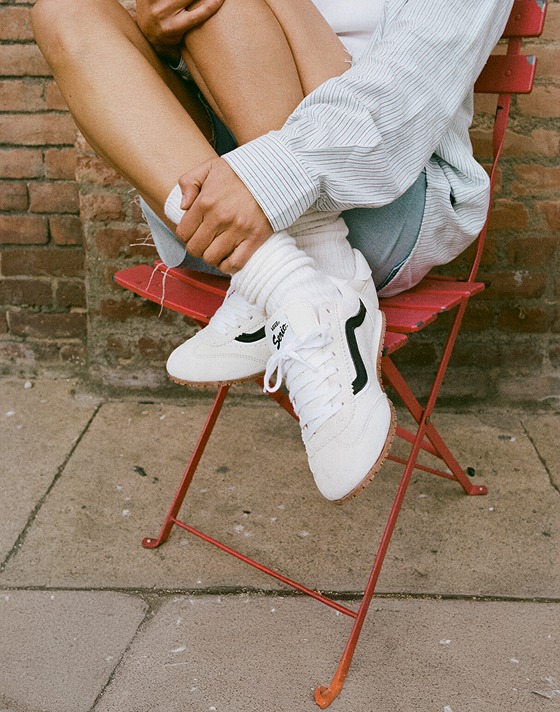 A woman sits in a red metal chair wearing white Super Lowpro shoes.