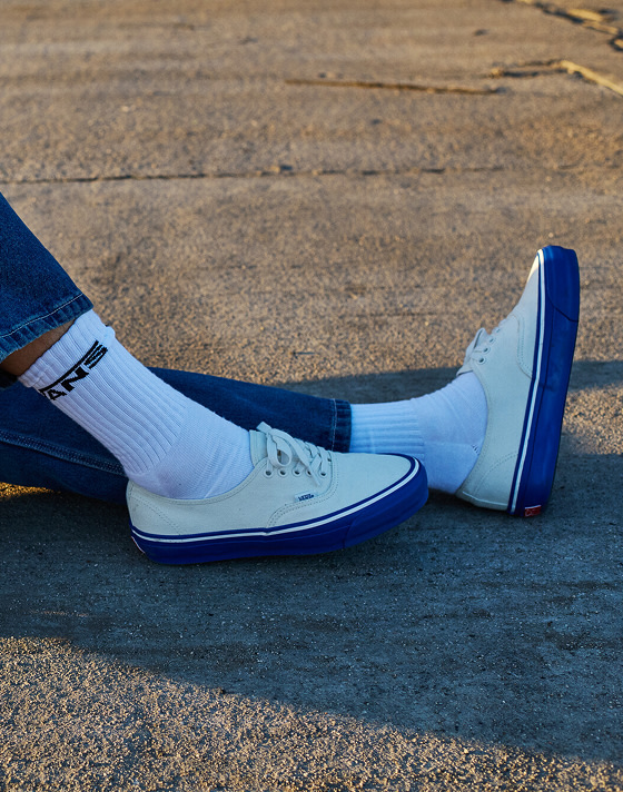Close-up of a man wearing white and blue Premium Authentic with white crew socks sitting on the concrete.