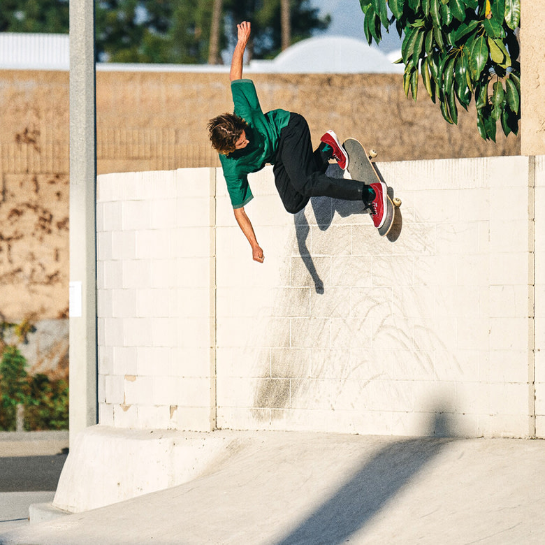Curren Caples riding a wall wearing a green polo, black jeans, and red Curren shoes.