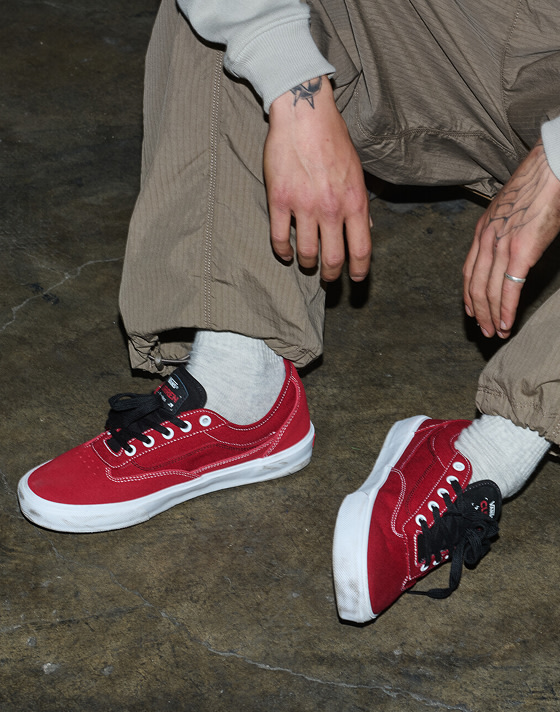 A close-up of a man sitting on concrete wearing red Curren shoes for an urban scene.