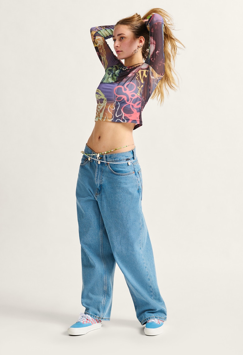 A woman tying her hair up in the Ludlow Mesh Long Sleeve Top and blue baggy denim jeans.