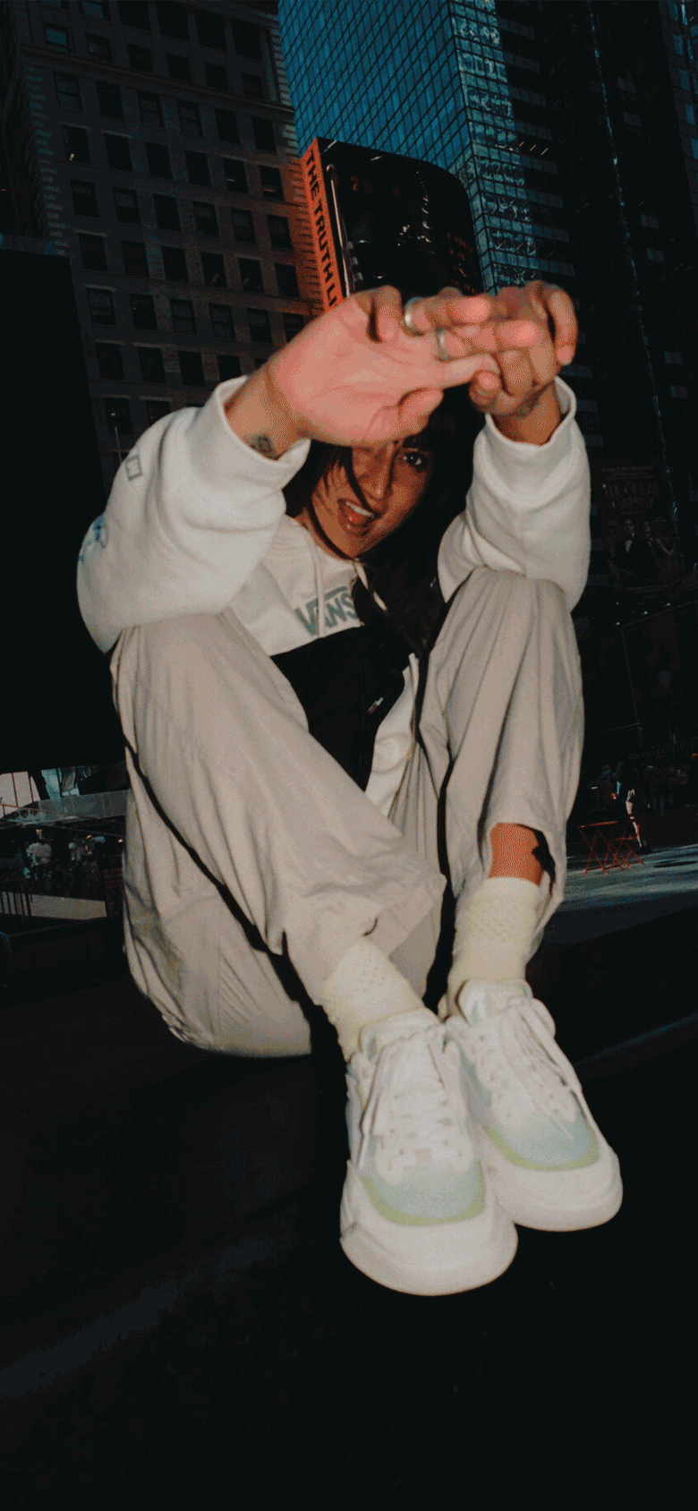 A trio of images: First, a young woman sits on the pavement with city buildings behind her, dressed in a Smokey Elevations Pullover Hoodie and All-New UltraRange 2.0 shoes, radiating relaxed urban style. The second is a black-and-white shot of a woman surfing in a Vans wetsuit, capturing motion and focus. The third shows two surfers walking toward the beach with boards in hand, both wearing UltraRange 2.0 shoes.